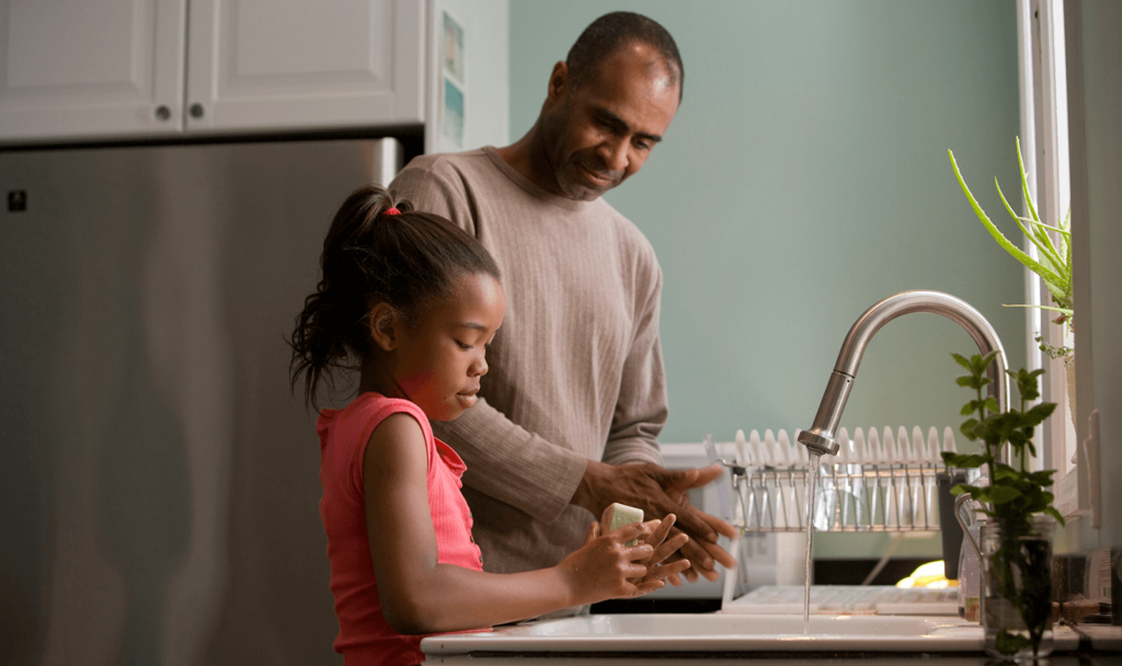 Father and daughter wash their hands at a kitchen sink